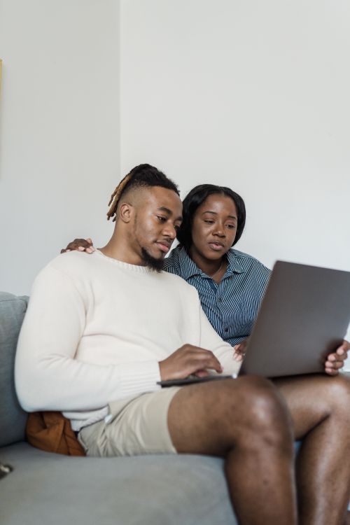 Free African American couple sitting on a couch using a laptop together, enjoying a cozy moment at home. Stock Photo
