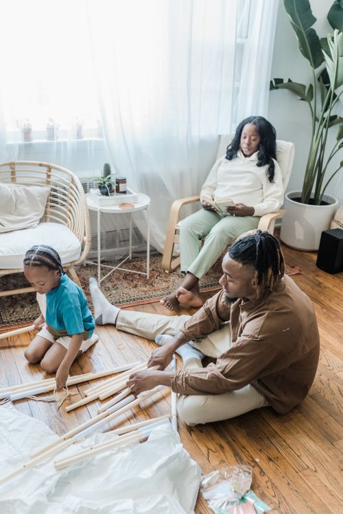 Free A father and son assembling a teepee while the mother relaxes in a sunlit living room. Stock Photo