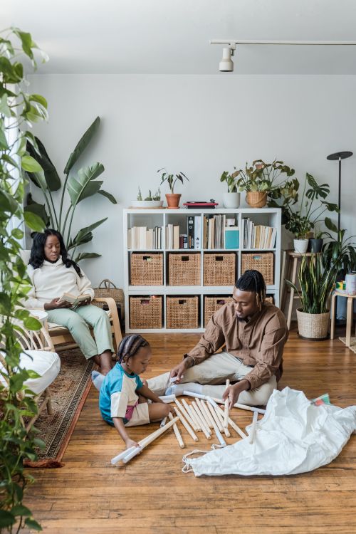 Free Father and child building a play tent at home while mother relaxes nearby in a cozy modern living room. Stock Photo