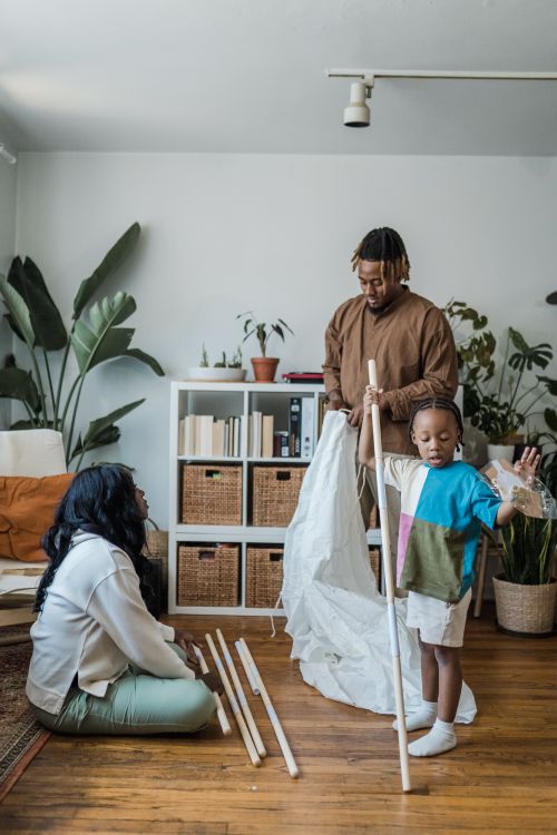 Free A family spends quality time assembling a tent in a cozy living room filled with plants and natural light. Stock Photo