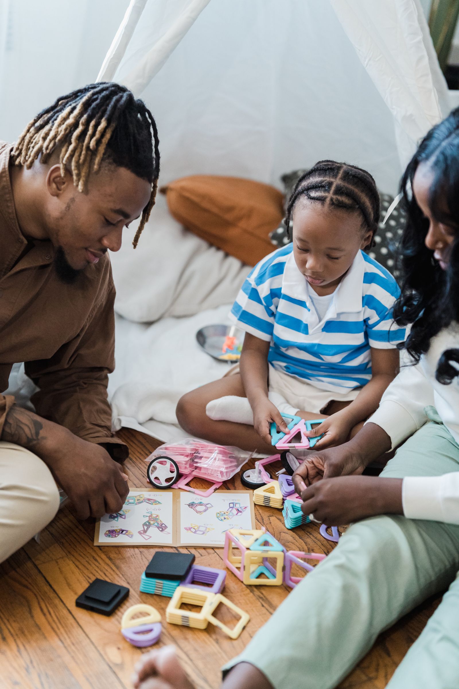 A family building a structure together with colorful magnetic tiles on the floor