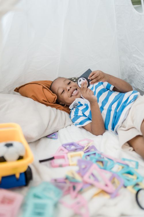 Free Cheerful child lying in a cozy indoor teepee with toys and smiling brightly. Stock Photo