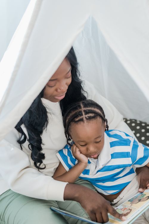 Free A mother and her child enjoy reading a book together under a cozy blanket at home. Stock Photo