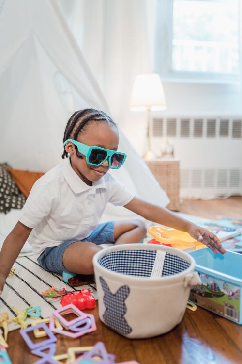 Free A cheerful child playing with colorful toys indoors, wearing sunglasses and enjoying playtime. Stock Photo