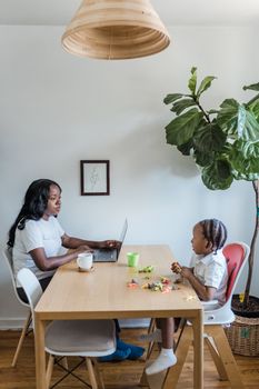 African American mother works while child plays at home in a cozy family setting.