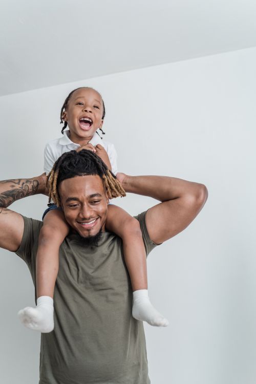 Free Father carrying his smiling child on shoulders, enjoying playful moment indoors. Stock Photo