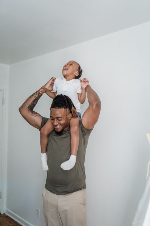 Free Happy father carrying his playful child on shoulders, enjoying fun moments indoors. Stock Photo