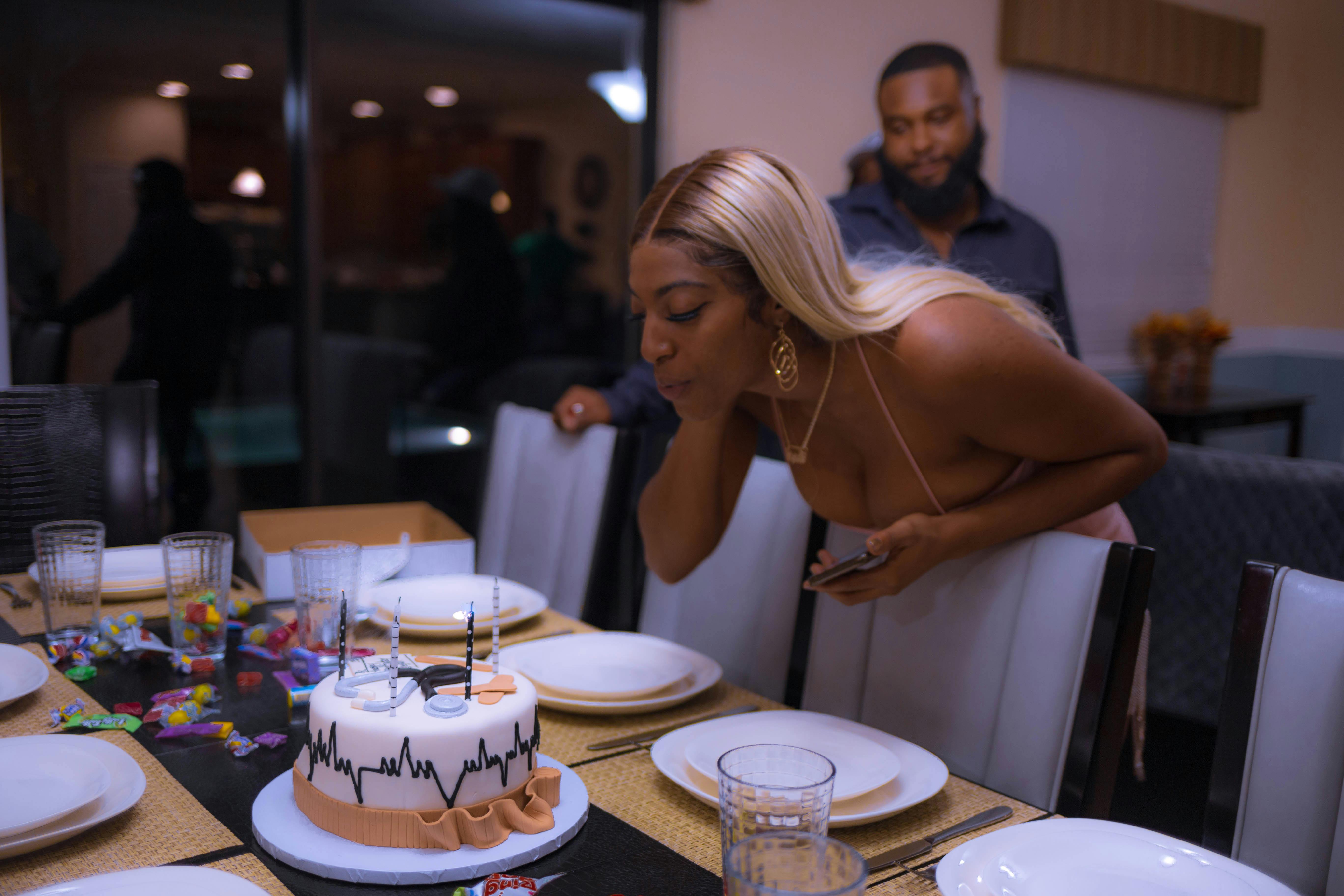 Woman blowing out candles on a decorated birthday cake at a stylish party setting.