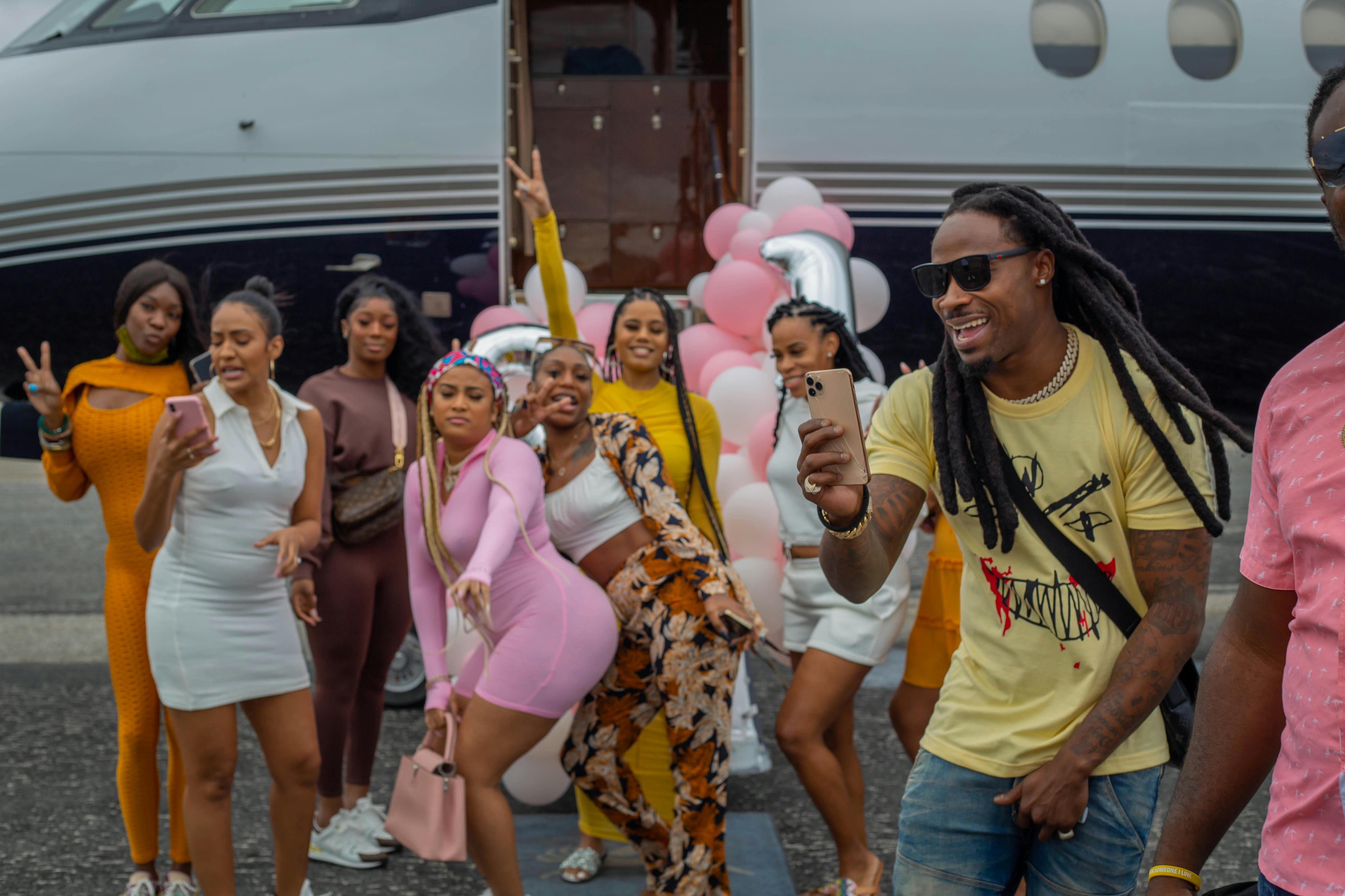 Group of joyful friends posing for selfies and celebrating near a private jet.