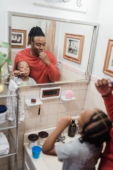 A joyful father and child brushing teeth together in a home bathroom mirror reflection.