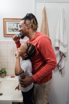 A father and son happily brush teeth together in a cozy bathroom.