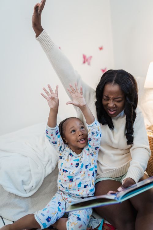 Free A joyful mother and child bonding while reading a book in a cozy bedroom setting, emphasizing family love and happiness. Stock Photo