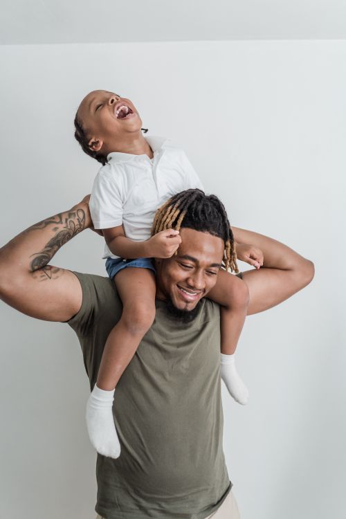 Free Father carrying son on shoulders, both laughing and enjoying the moment indoors. Stock Photo