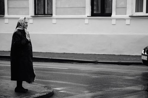 Free A black and white photo of an elderly woman crossing a wet road in Grodno, Belarus. Stock Photo