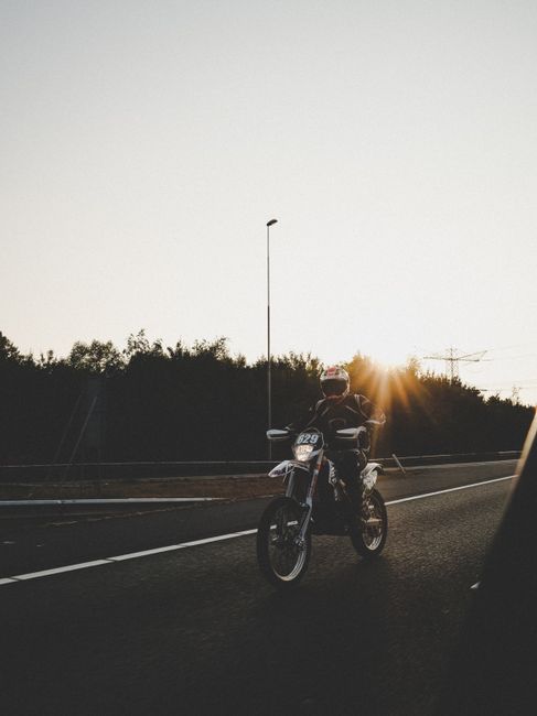A motorcyclist wearing a helmet rides on an open road during sunset, creating a striking silhouette.