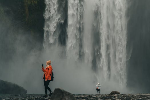 Two tourists admire the majestic Skogafoss waterfall in Iceland, capturing the moment in nature's beauty.