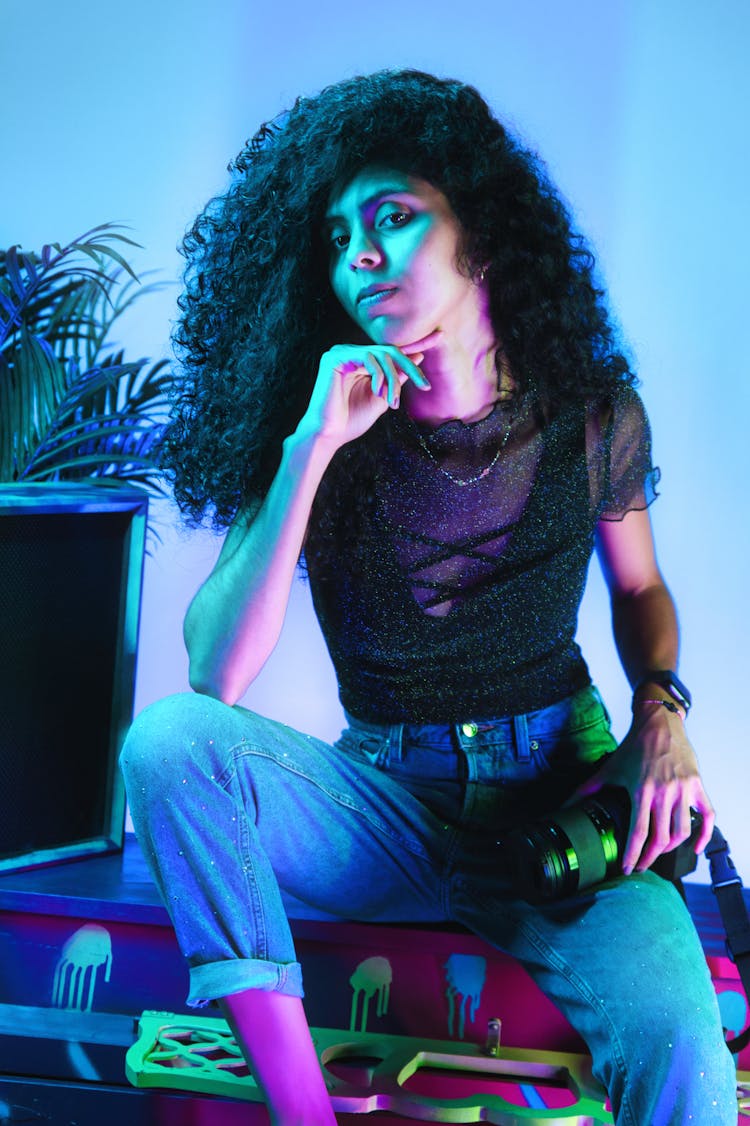 A Woman Wearing Black Shirt And Denim Pants In A Blue Lighting Holding A Camera