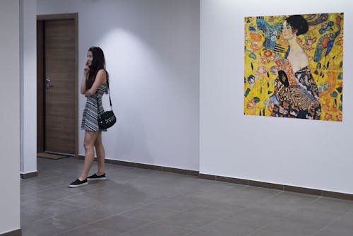 여러 여자 그림으로 흰 벽 근처에 서있는 여자
