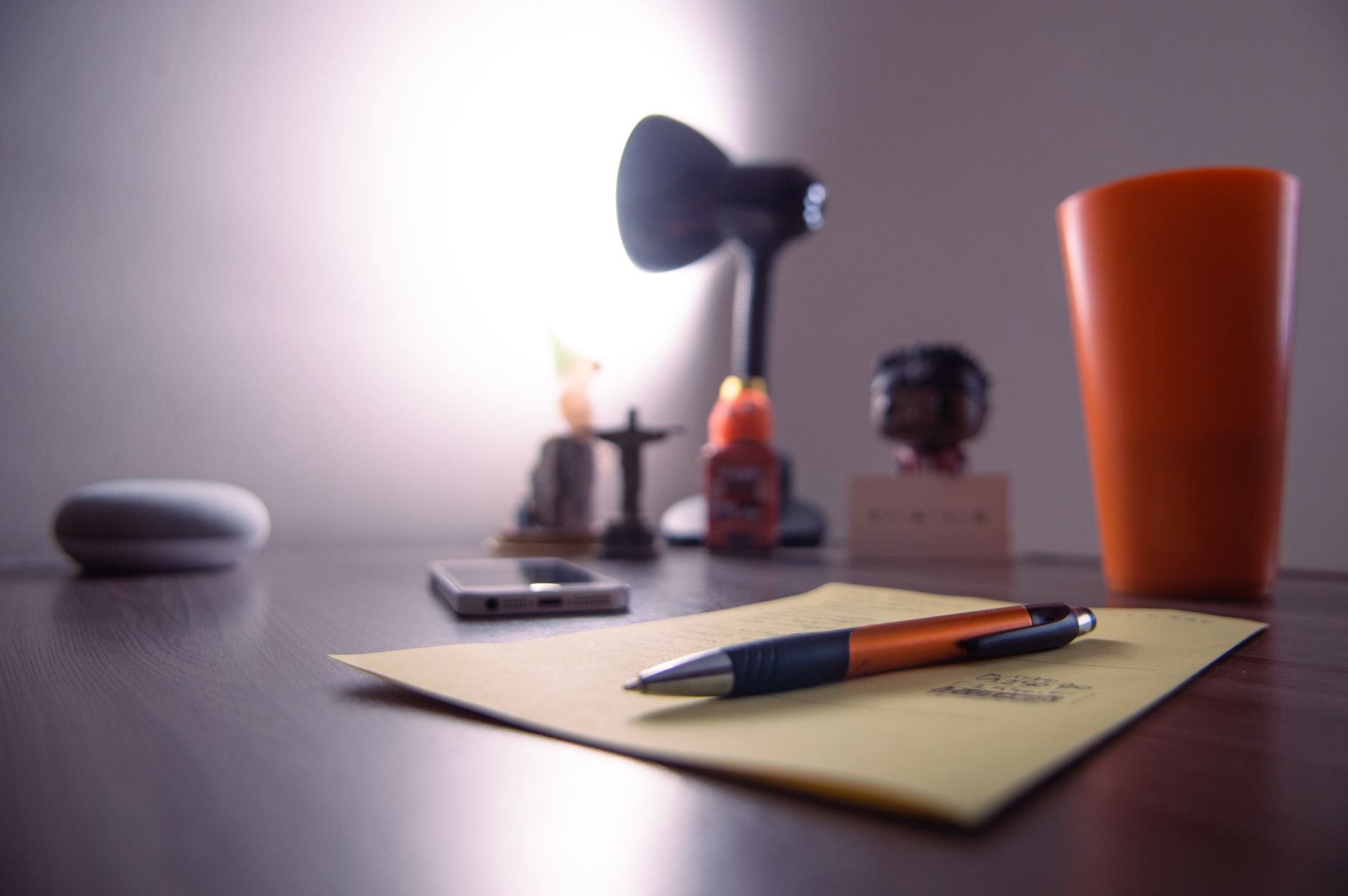 Close-up view of a desk with a pen, notepad, lamp, smartphone, and decorative items, creating a cozy workplace ambiance.