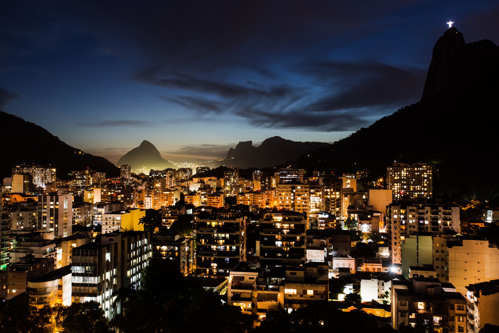 Night view of Rio de Janeiro's city lights with iconic landmarks under a serene sky.