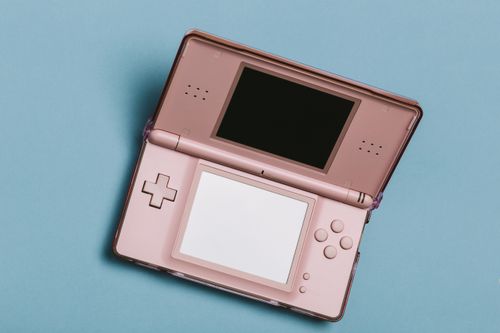 Free Close-up of a pink portable gaming console with dual screens on a blue surface. Stock Photo