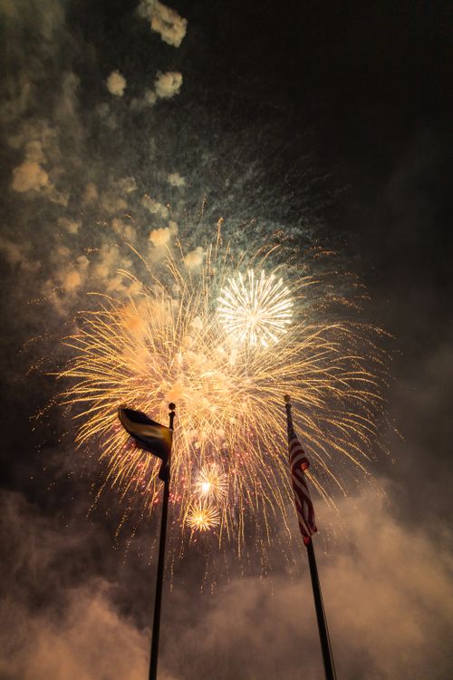 Free Stunning fireworks bursting in the night sky with the American flag waving below, perfect for festive celebrations. Stock Photo