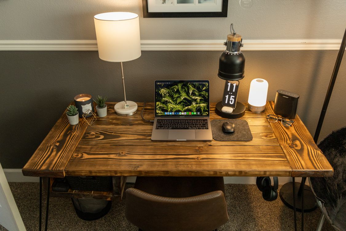 Escritório doméstico com notebook, luminárias e poucos objetos decorativos sobre a mesa