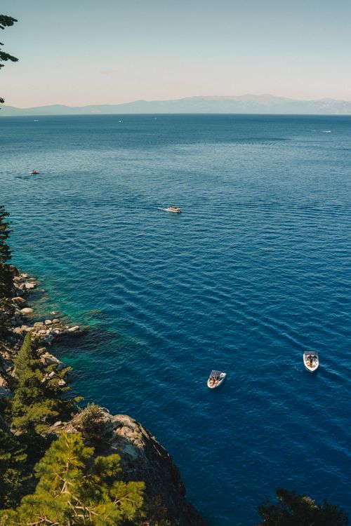 Free A captivating high-angle view of boats sailing on tranquil blue waters near a rocky coastline dotted with green trees. Ideal for travel and nature themes. Stock Photo