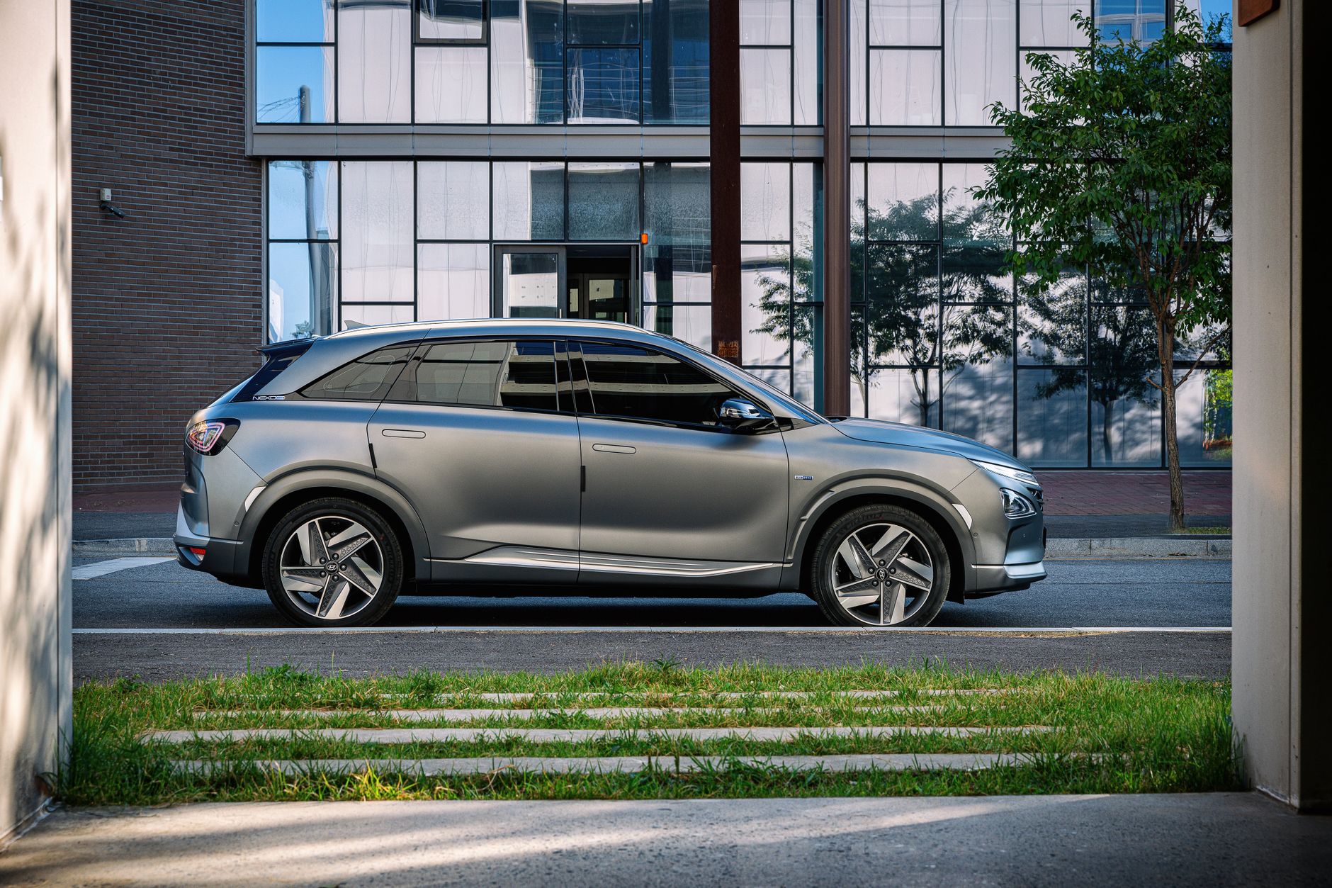 Side view of a sleek gray SUV parked beside a glass building in an urban setting.