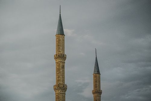 Free Two majestic minarets tower against a dramatic overcast sky, symbolizing Islamic architecture and faith. Stock Photo