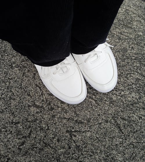 A Person in Black Pants Wearing White Sneakers while Standing on the Ground