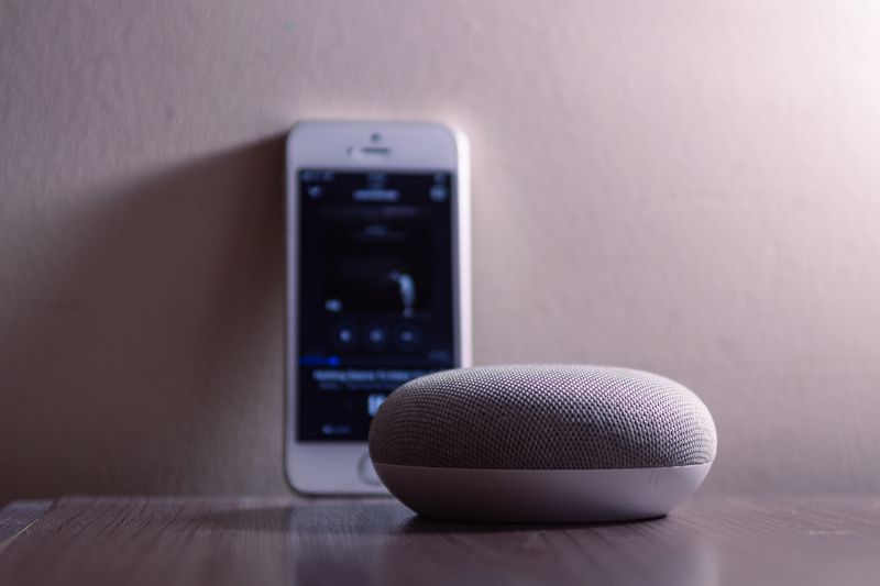 A modern smart speaker and smartphone on a wooden table, indoors.