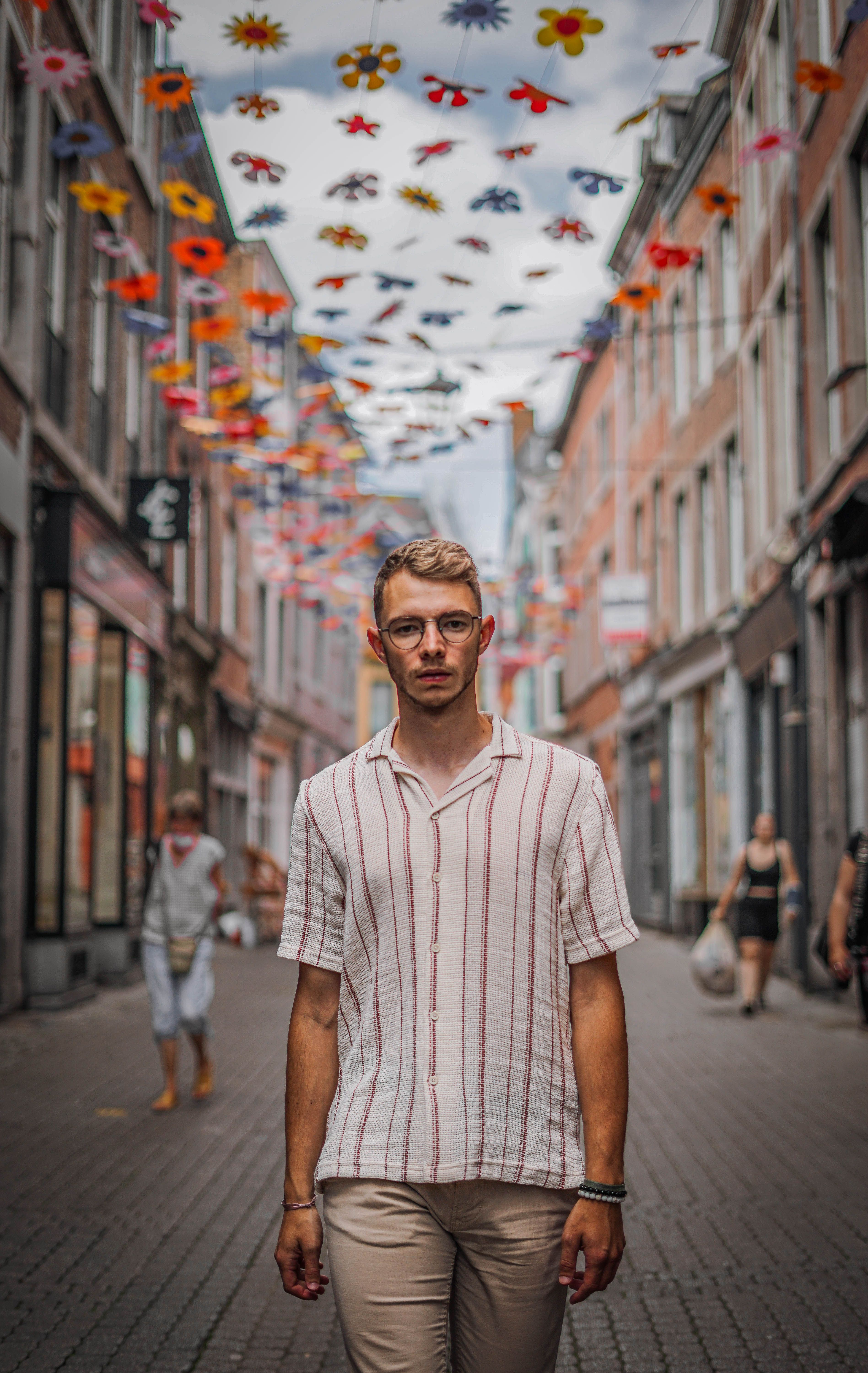 A man wearing a striped shirt walks down a cobblestone street adorned with colorful decorations in Namur, Belgium.