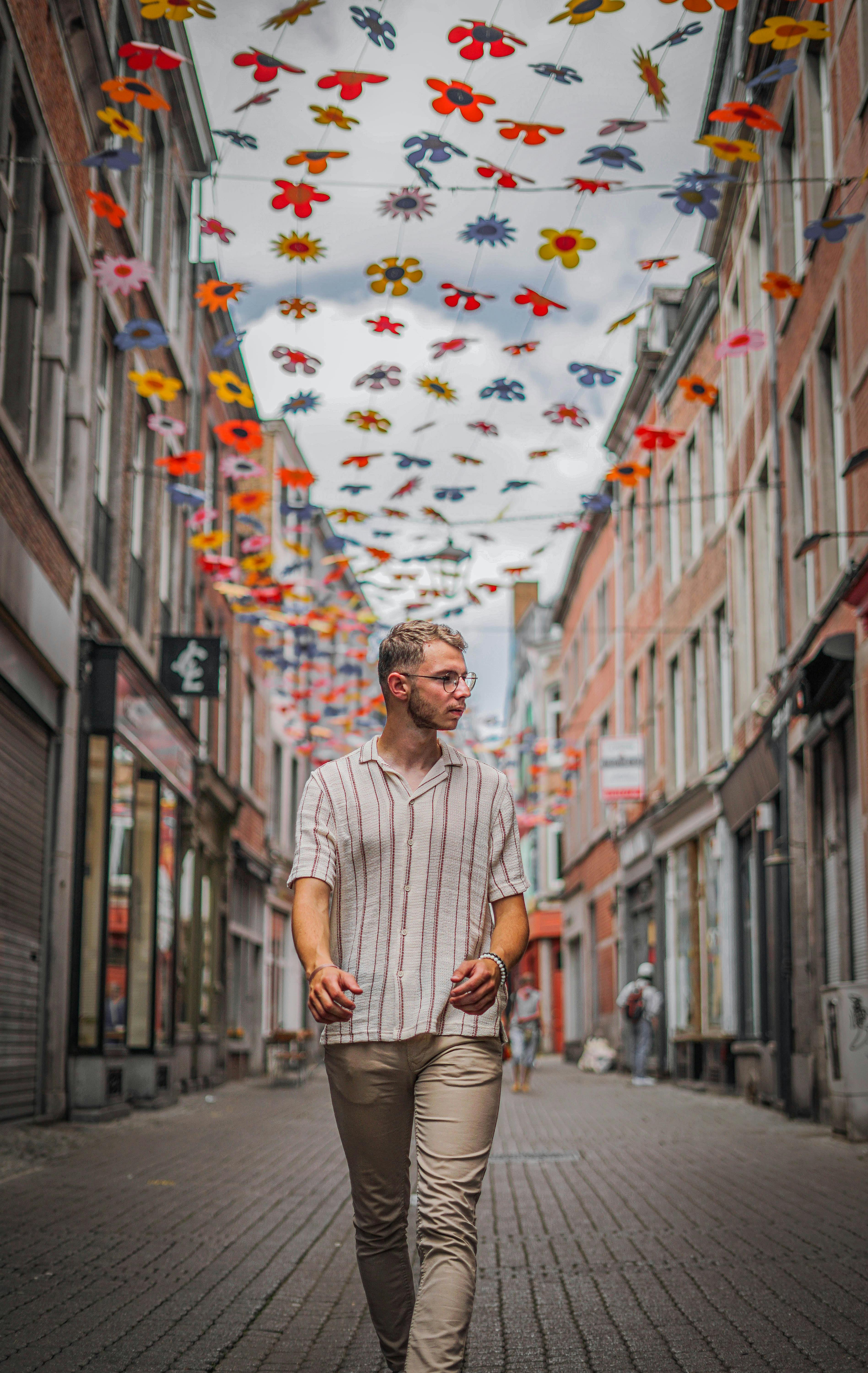 A man walks along a decorated pedestrian street in Namur, Belgium, with vibrant overhead decor.
