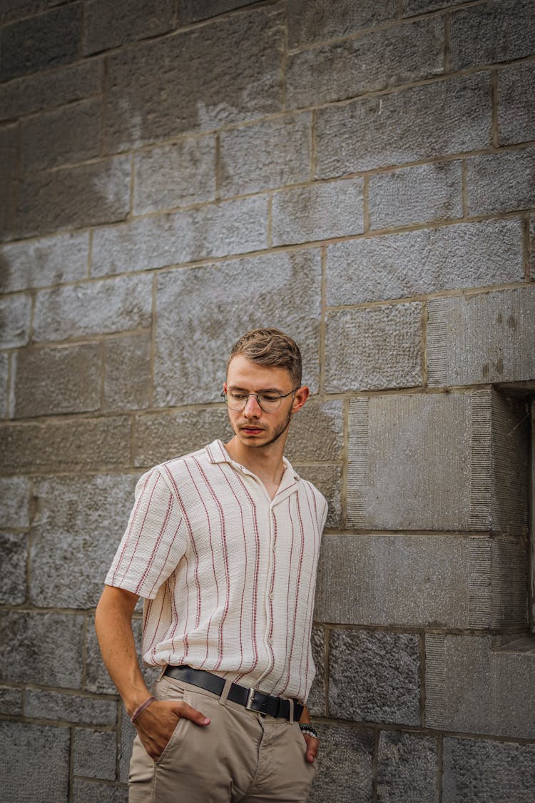 Young Blonde Man In Shirt And Pants Standing By Building Wall 