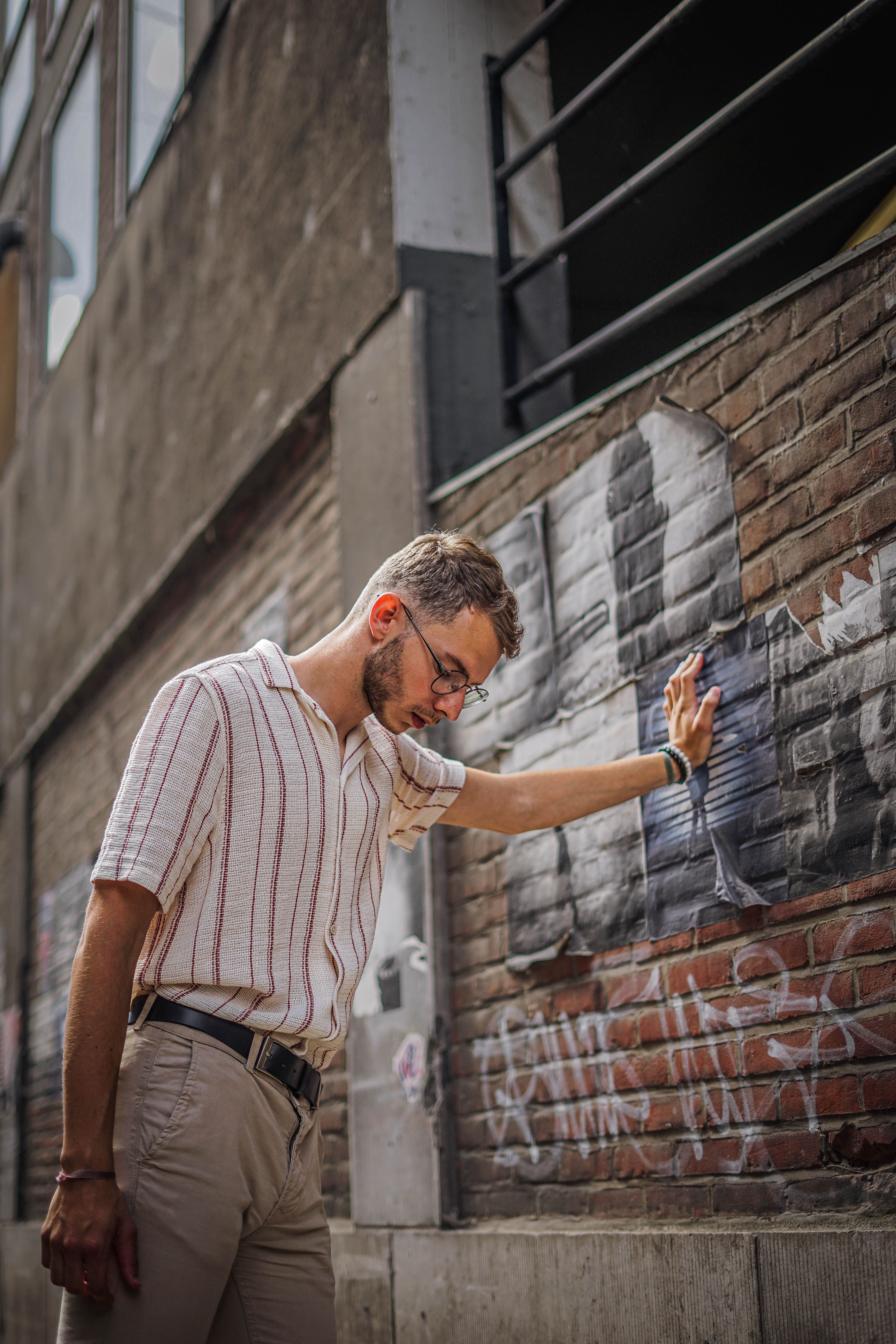 Young man in striped shirt leans against urban graffiti brick wall in Namur, Belgium.