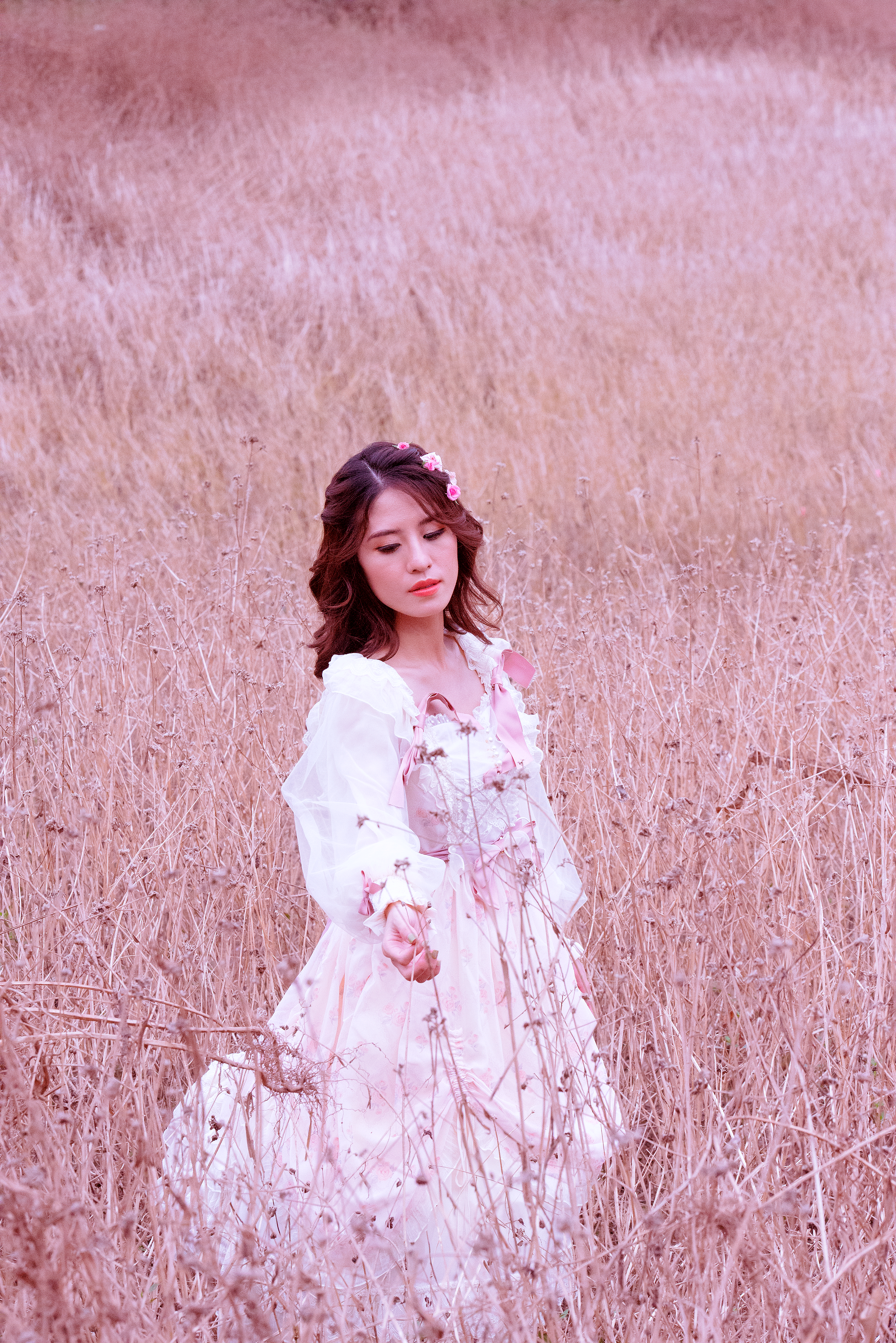 Elegant woman in white dress standing in a serene grass field, exuding beauty and calmness.