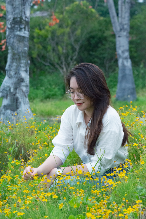 Free Asian woman enjoying nature, sitting among yellow flowers outdoors. Stock Photo