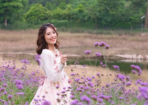 Beautiful Woman in White Dress near Purple Flowers