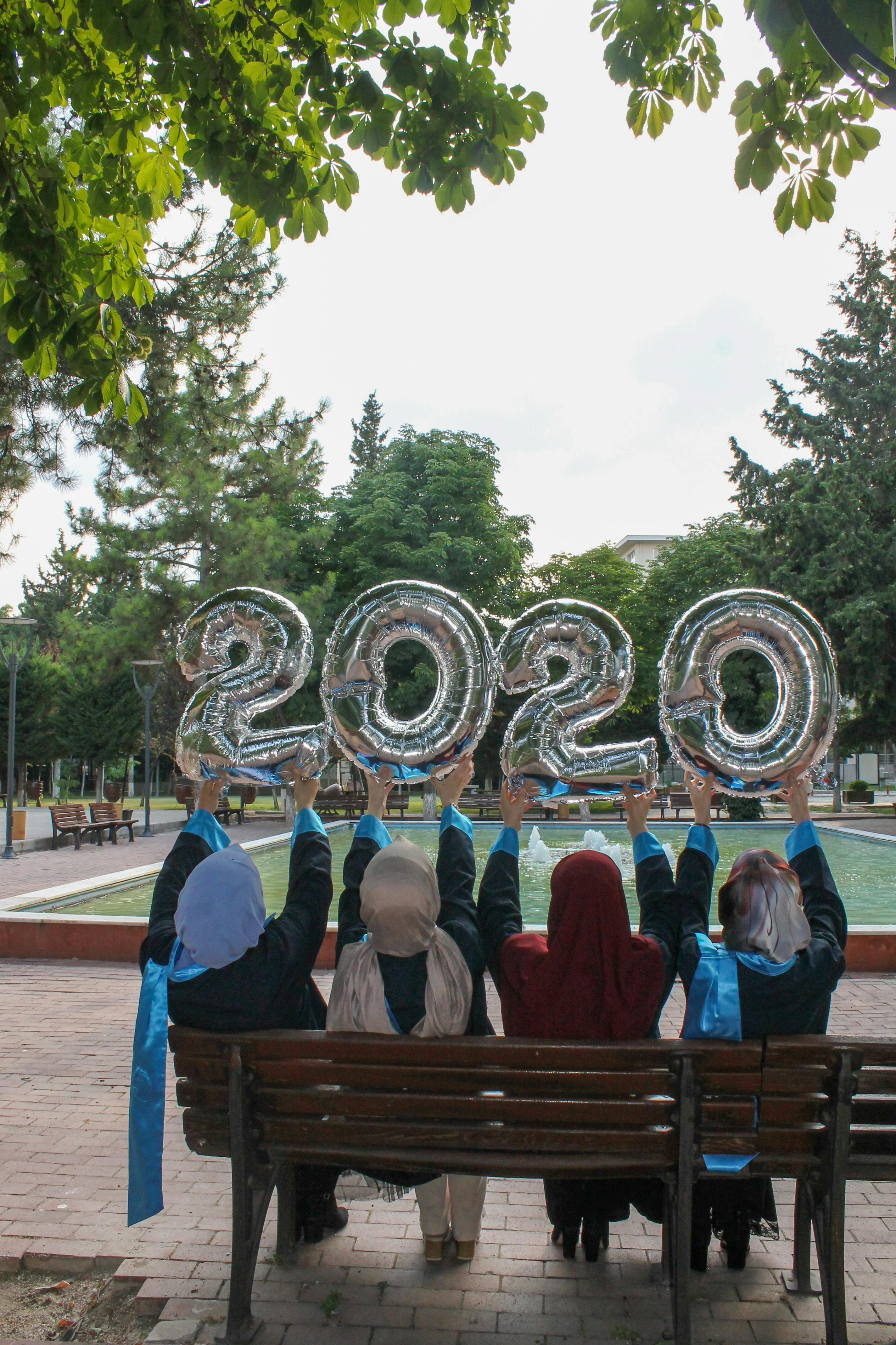 back view of women sitting on a wooden bench holding balloons