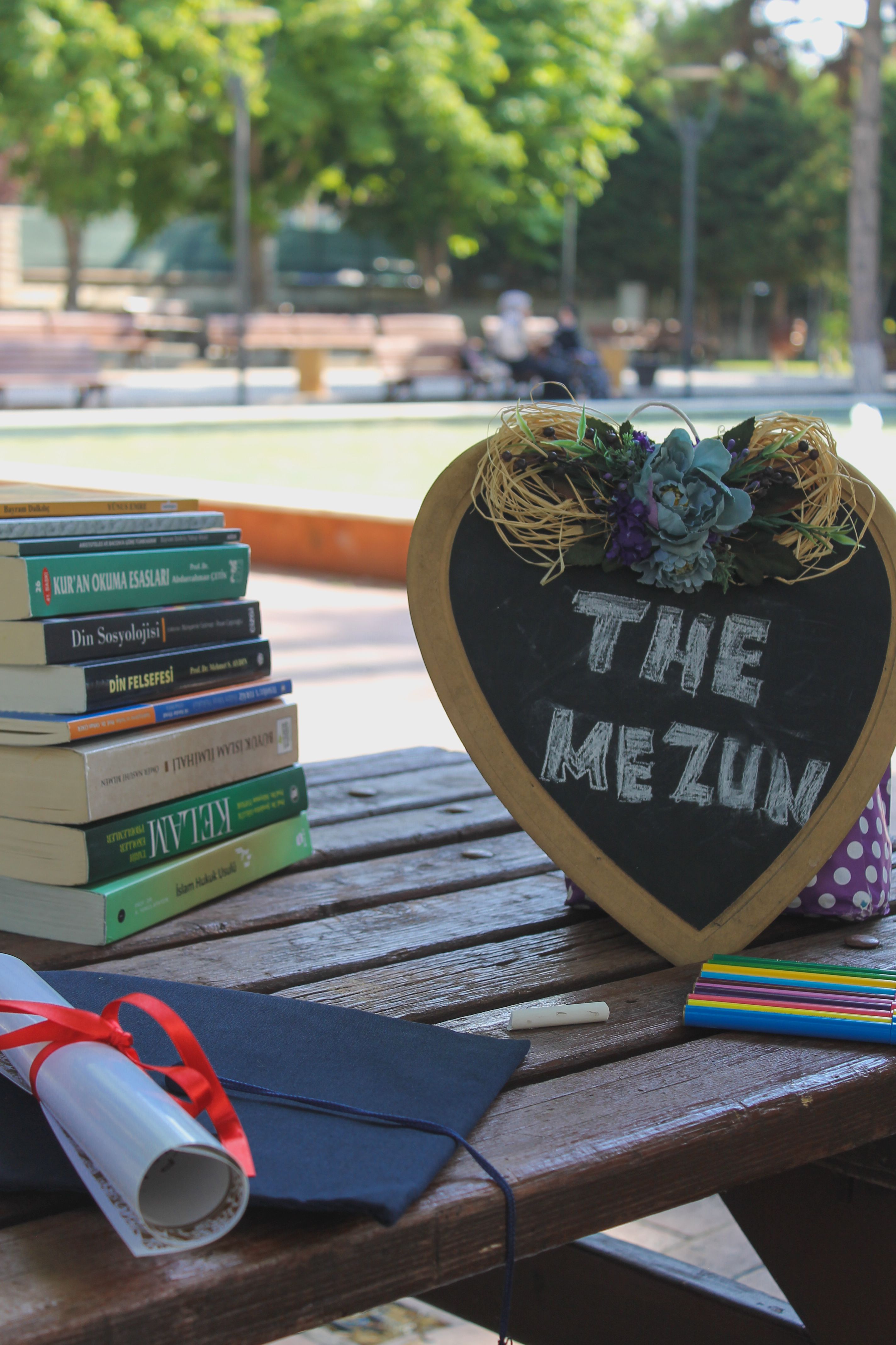 Graduation-themed outdoors setup featuring books, blackboard, and diploma on a wooden table.