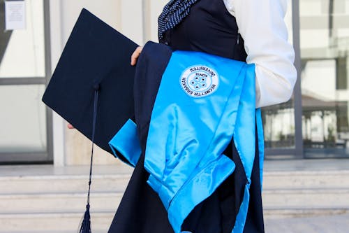 Close-Up Shot of a Person Holding Graduation Gown and Square Academic Cap