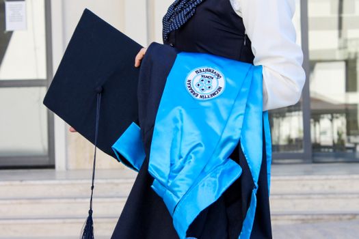 Close-up of a person in graduation attire holding a cap and gown outside a building.