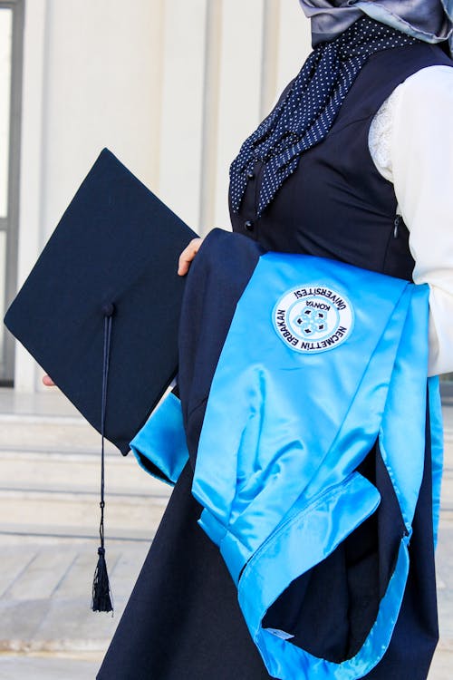 Close-Up Shot of a Person Holding Graduation Gown and Academic Cap