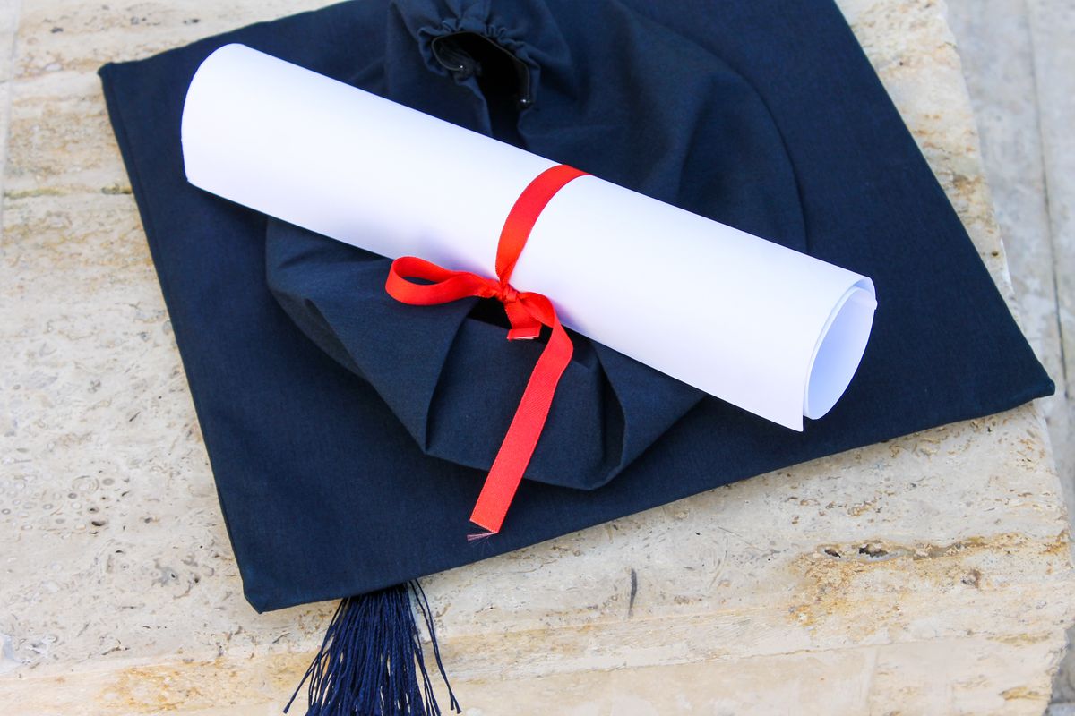 Graduation cap with diploma roll tied with red ribbon on concrete surface