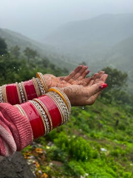 Close-up of henna hands with red bangles in a rainy Panchgani landscape.