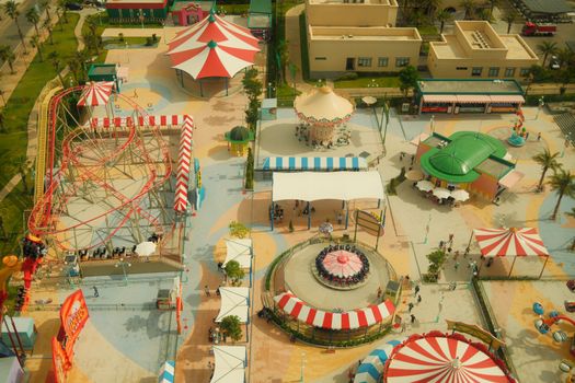 High-angle aerial view of colorful amusement park rides during day, showcasing roller coasters and carousels.