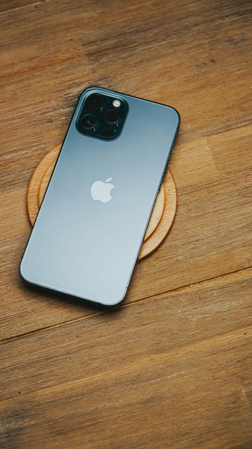 Free High-angle view of a sleek smartphone resting on a wooden table, showcasing modern technology design. Stock Photo