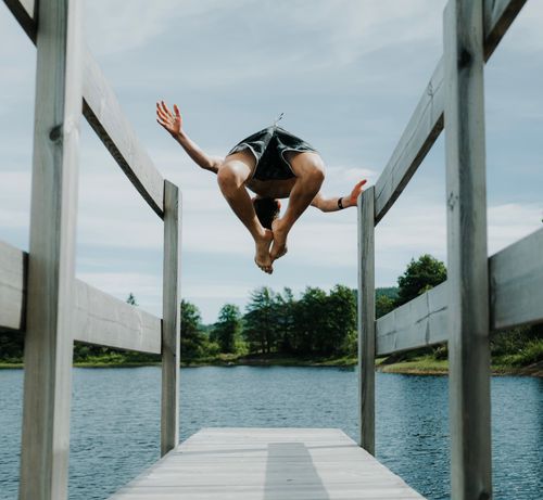 Free A teenager joyfully jumps off a wooden dock into a serene lake during summer. Stock Photo