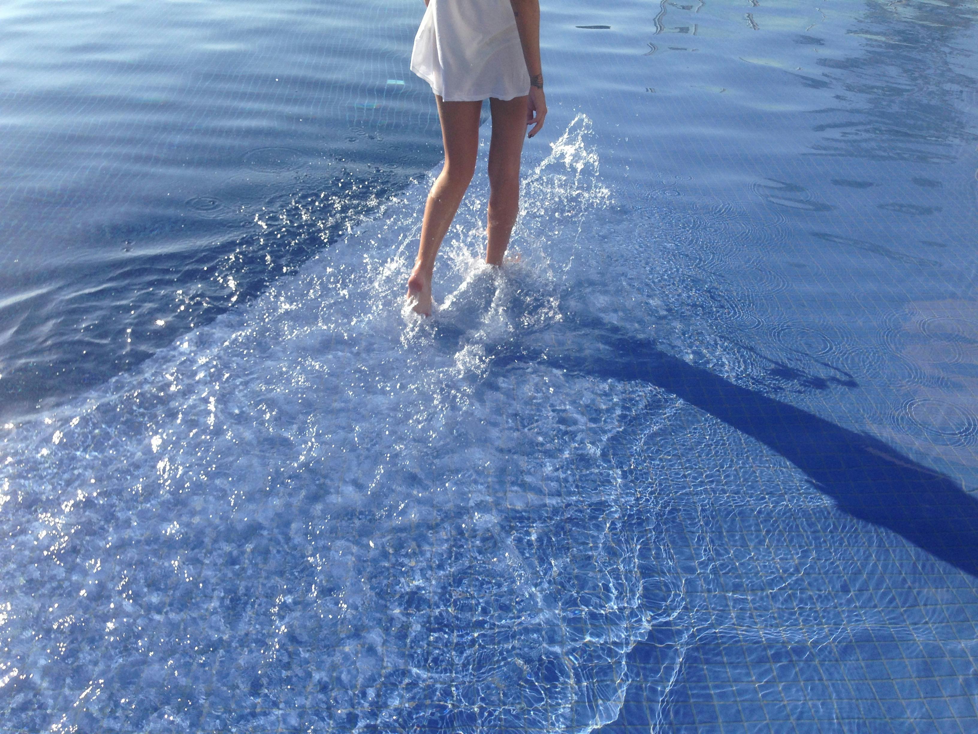 A woman in a white dress walking through shallow pool waters, capturing a moment of relaxation and fun.